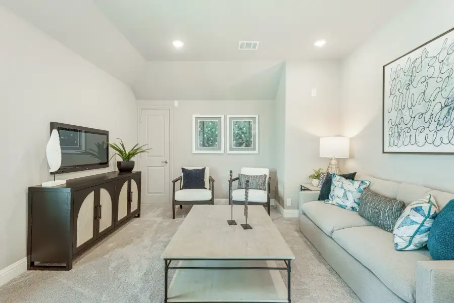 Living room with gray sofa, teal accent pillows, TV console, two accent chairs, and carpeted floors