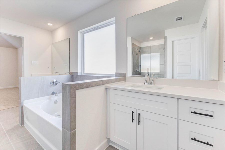 Crisp and clean, the primary bathroom boasts a dual vanity, deep soaking tub, and oversized mirror. A large frosted window over the tub brings in soft light, creating a spa-like retreat designed for everyday relaxation. Crisp and clean, the primary bathroom boasts a dual vanity, deep soaking tub, and oversized mirror. A large frosted window over the tub brings in soft light, creating a spa-like retreat designed for everyday relaxation.