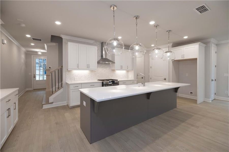 Kitchen with pendant lighting, white cabinetry, an island with sink, and wall chimney exhaust hood