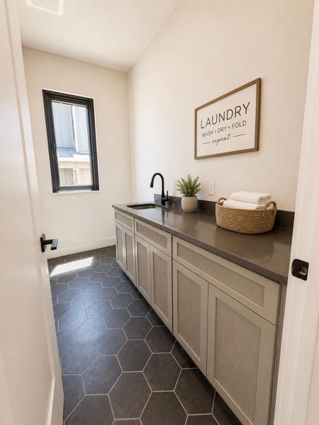 A well-appointed laundry area features practical counter space, an integrated sink, and hexagon tile flooring.