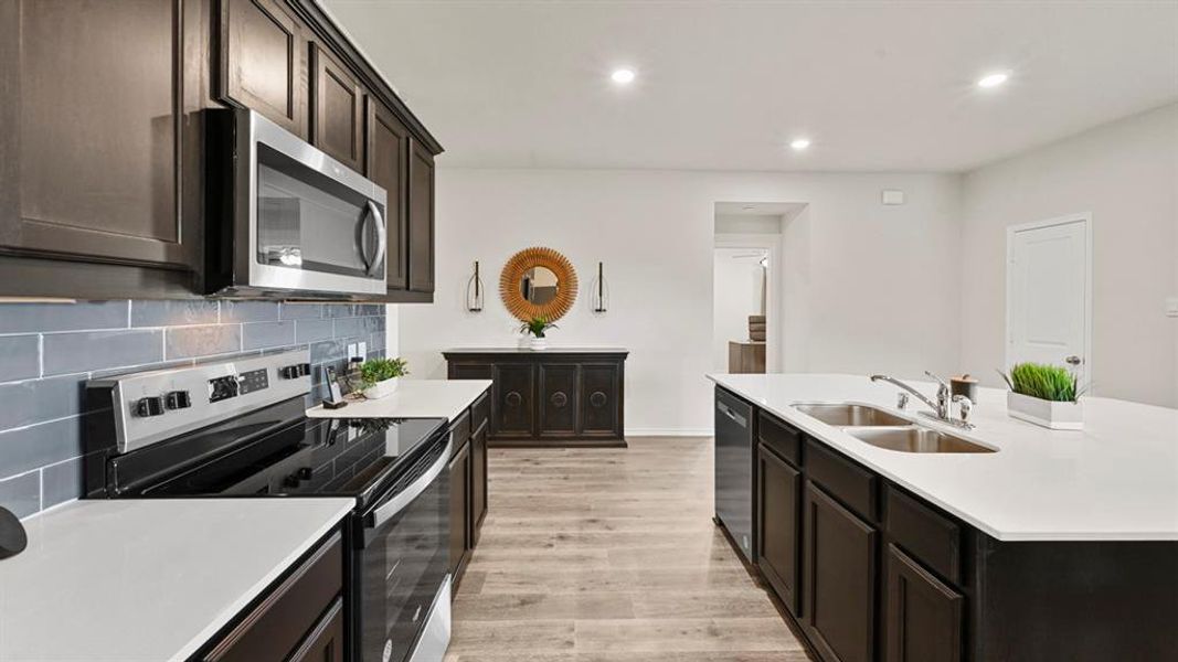 The kitchen features dark cabinetry, stainless steel appliances, a grey subway tile backsplash, and an island with a double basin sink