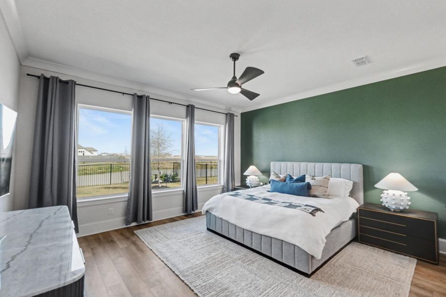 The luxurious primary suite offers a serene retreat with a calm green accent wall. The expansive windows look out to the backyard with a water view.