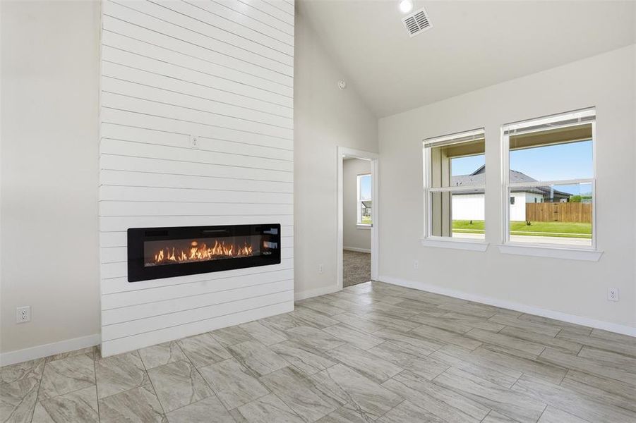 Living area featuring a floor-to-ceiling shiplap accent wall with a built-in linear electric fireplace, two large windows, wood-finish tile flooring, and vaulted ceiling