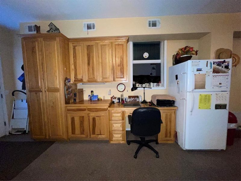 Kitchen with built in desk, refrigerator, and dark colored carpet Kitchen with built in desk, refrigerator, and dark colored carpet