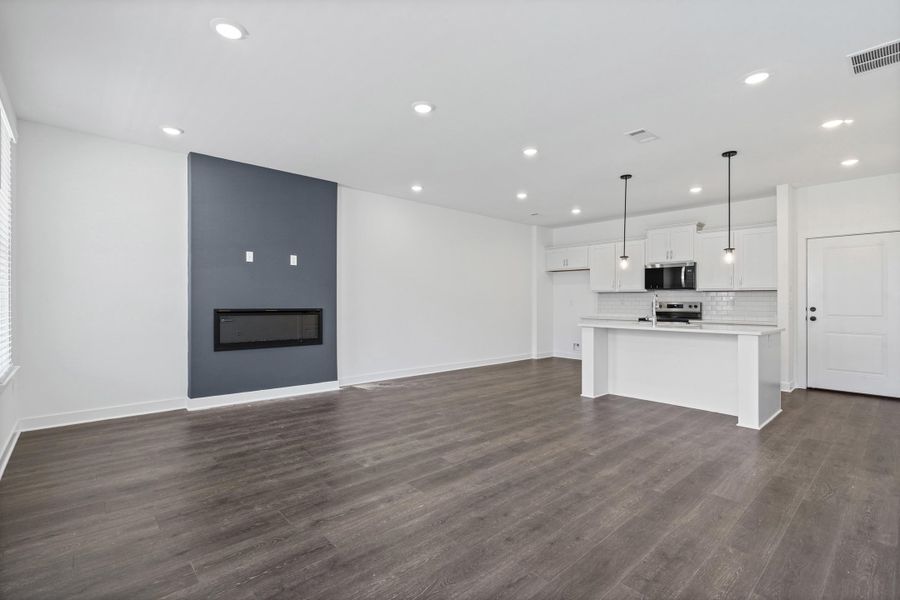 Open-concept living area featuring wood-finish flooring, recessed lighting, and a modern fireplace with a dark accent wall