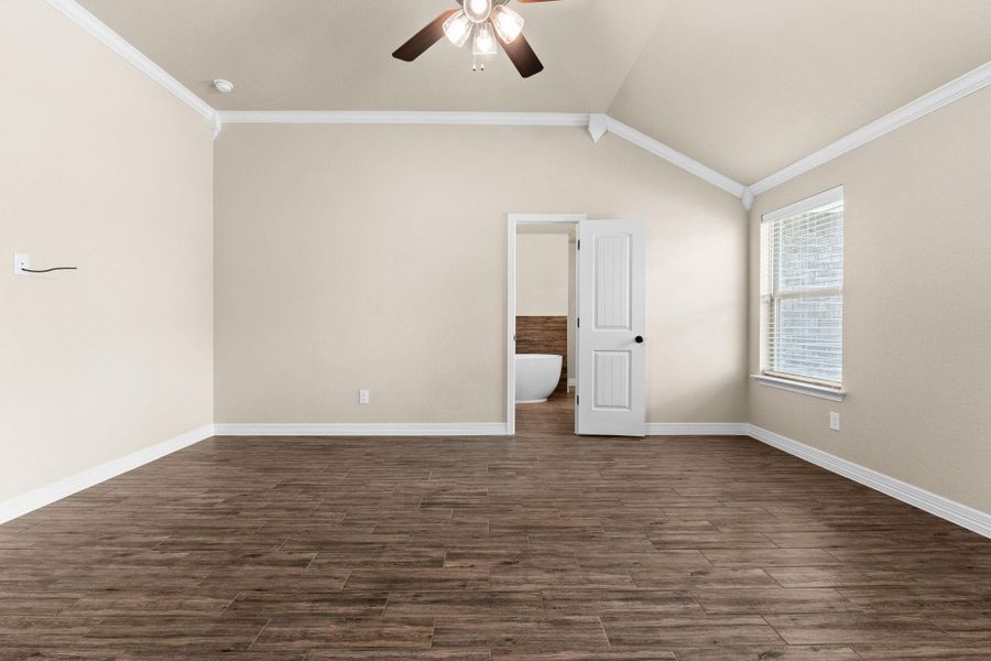 Empty room featuring crown molding, dark wood like tile floors, lofted ceiling, and a ceiling fan Empty room featuring crown molding, dark wood like tile floors, lofted ceiling, and a ceiling fan