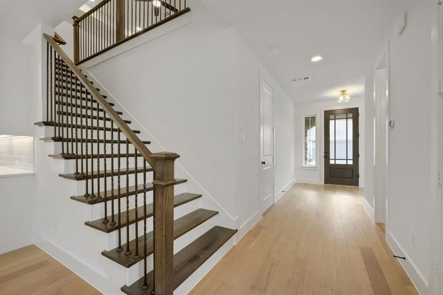 Entry foyer featuring light wood-finish flooring, a dark wood-paneled front door with multiple glass lites, a complementing staircase with dark wood treads and wrought iron balusters, and recessed ceiling lighting Entry foyer featuring light wood-finish flooring, a dark wood-paneled front door with multiple glass lites, a complementing staircase with dark wood treads and wrought iron balusters, and recessed ceiling lighting