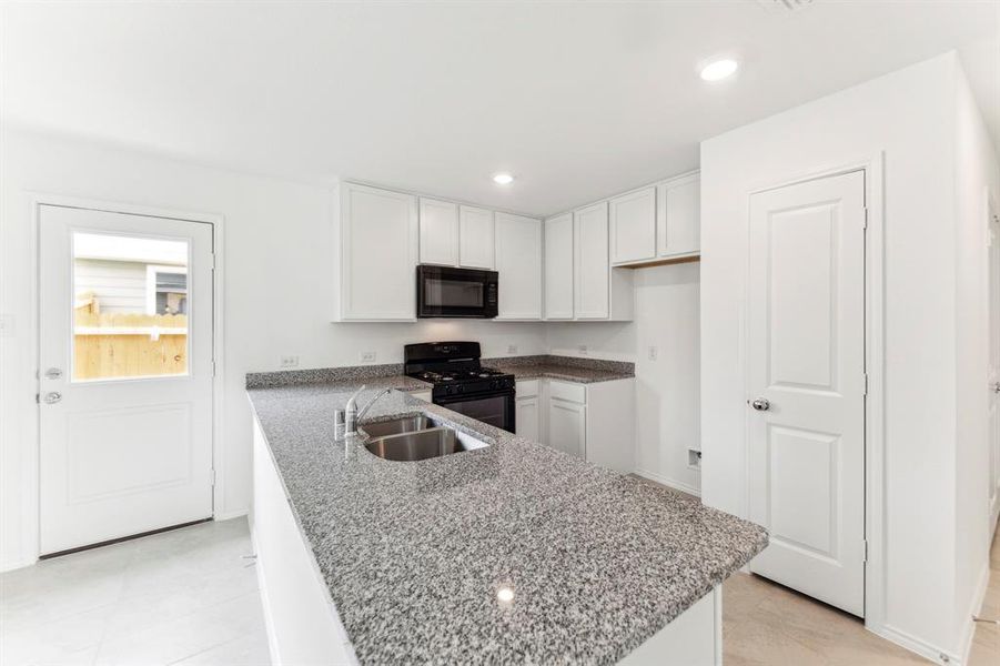 Kitchen with black appliances, white cabinets, sink, light stone countertops, and light tile patterned floors