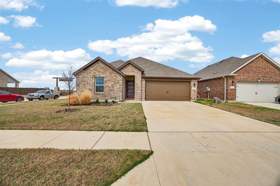 View of front facade featuring a garage, brick siding, concrete driveway, roof with shingles, and a front lawn