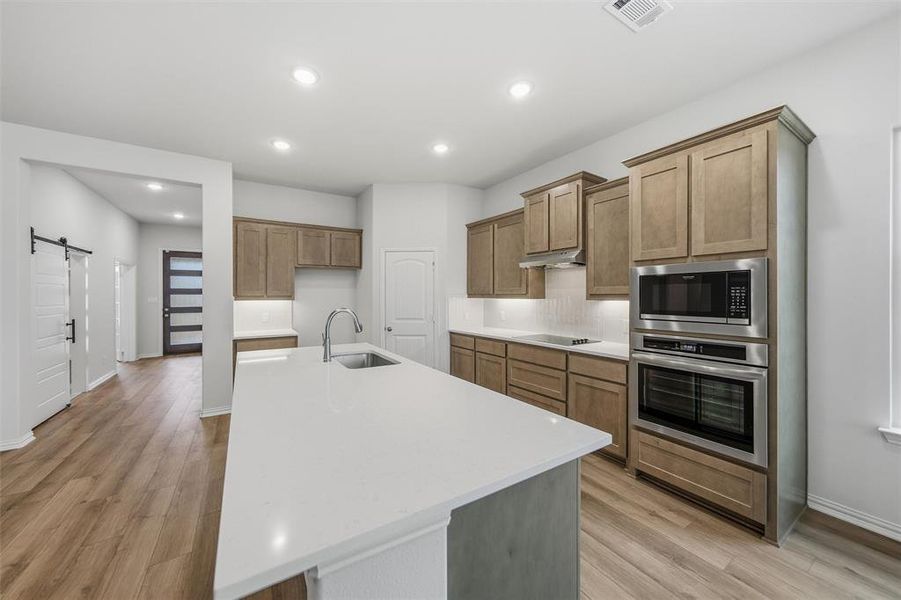 Kitchen with a barn door, wood finish cabinets, stainless steel appliances, light stone counters, and decorative backsplash Kitchen with a barn door, wood finish cabinets, stainless steel appliances, light stone counters, and decorative backsplash