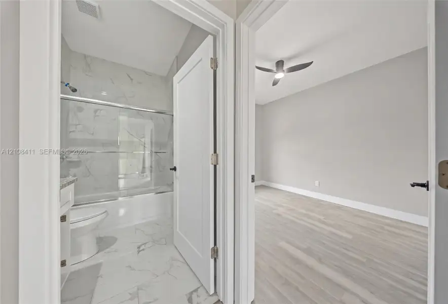Full bathroom with a tub-shower combination featuring tile surround, and an interior room with wood-finish flooring and a ceiling fan