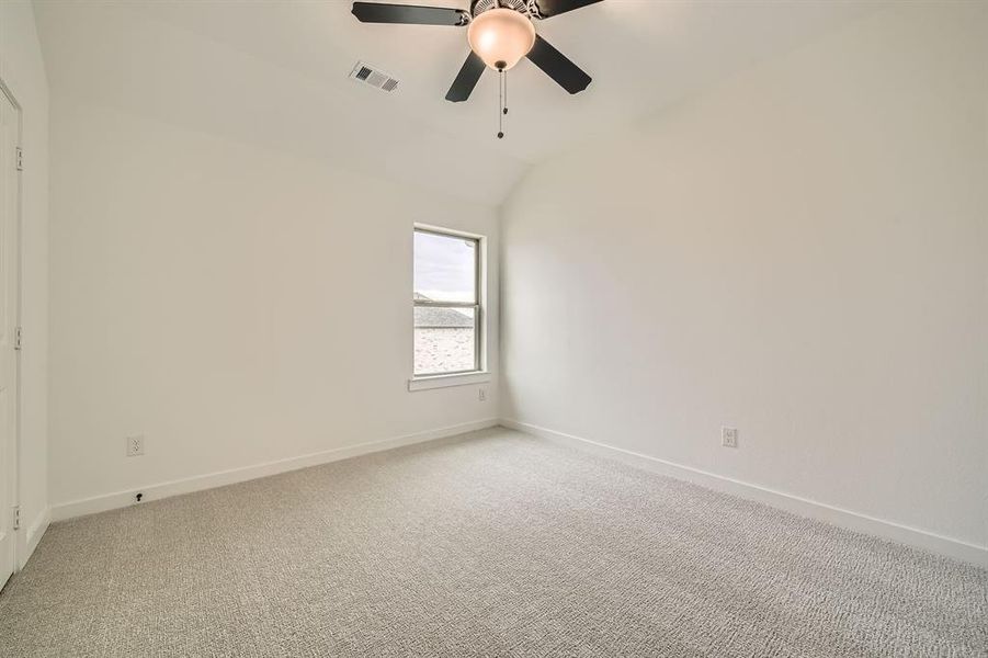 Carpeted empty room featuring ceiling fan and vaulted ceiling