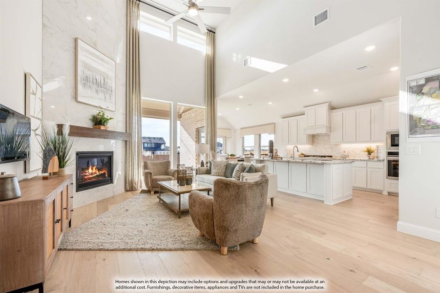 Open-concept living room with two-story ceiling, marble fireplace, and view into white kitchen with island Open-concept living room with two-story ceiling, marble fireplace, and view into white kitchen with island