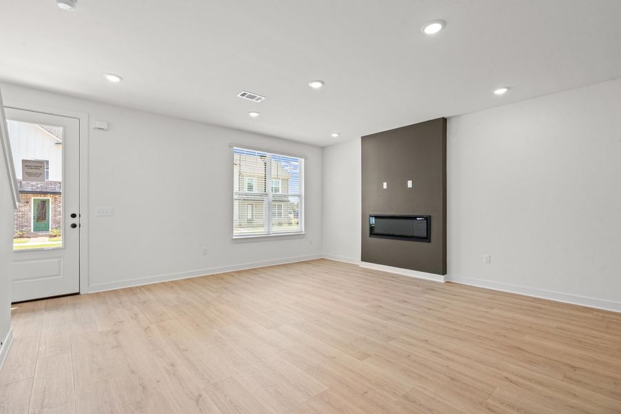 Recessed lighting illuminates the open living area featuring wood-finish flooring, an electric fireplace with a dark accent wall, and a large window
