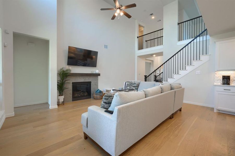 Living room featuring ceiling fan, a towering ceiling, light hardwood / wood-style floors, and a fireplace