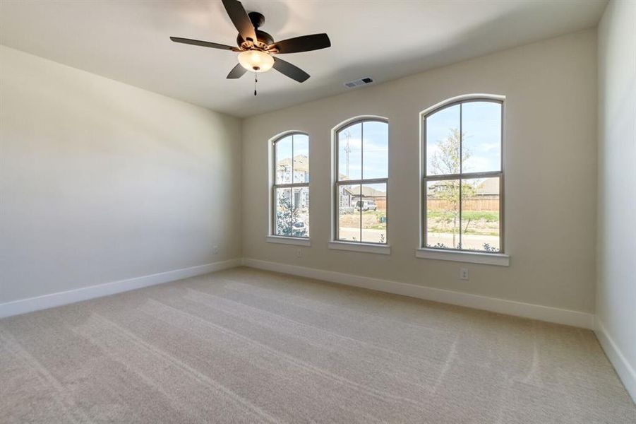 Empty room featuring light colored carpet, a ceiling fan, and healthy amount of natural light Empty room featuring light colored carpet, a ceiling fan, and healthy amount of natural light