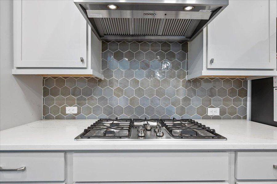 Kitchen with wall chimney range hood, stainless steel gas cooktop, light stone counters, and white cabinets