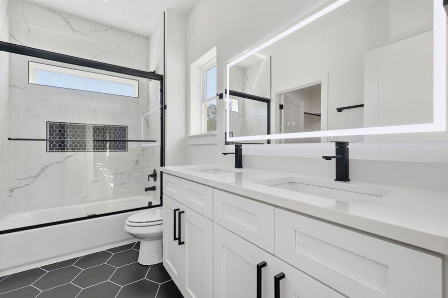 Bathroom with enclosed tub / shower combo, double vanity, and dark tile patterned flooring