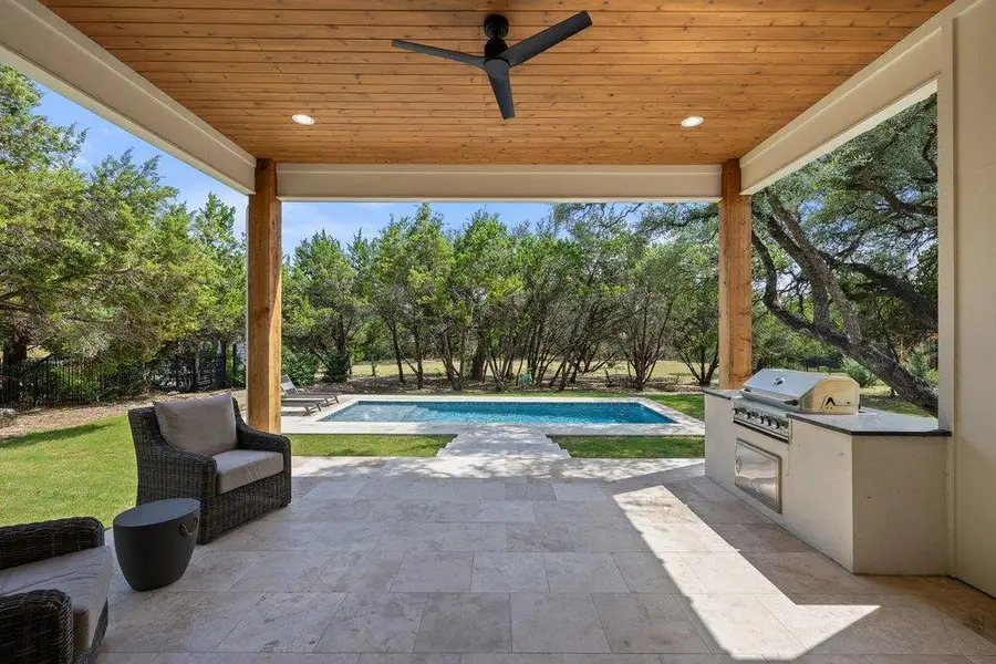 An inviting covered patio offers a luxurious outdoor kitchen and a serene pool set against a lush, green backdrop. An inviting covered patio offers a luxurious outdoor kitchen and a serene pool set against a lush, green backdrop.