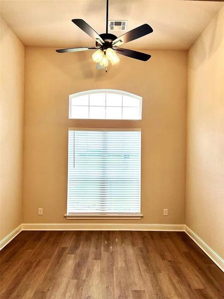 Spacious room featuring vaulted ceilings, wood-finish flooring, a contemporary ceiling fan with integrated lighting, and a combination of arched and rectangular windows Spacious room featuring vaulted ceilings, wood-finish flooring, a contemporary ceiling fan with integrated lighting, and a combination of arched and rectangular windows