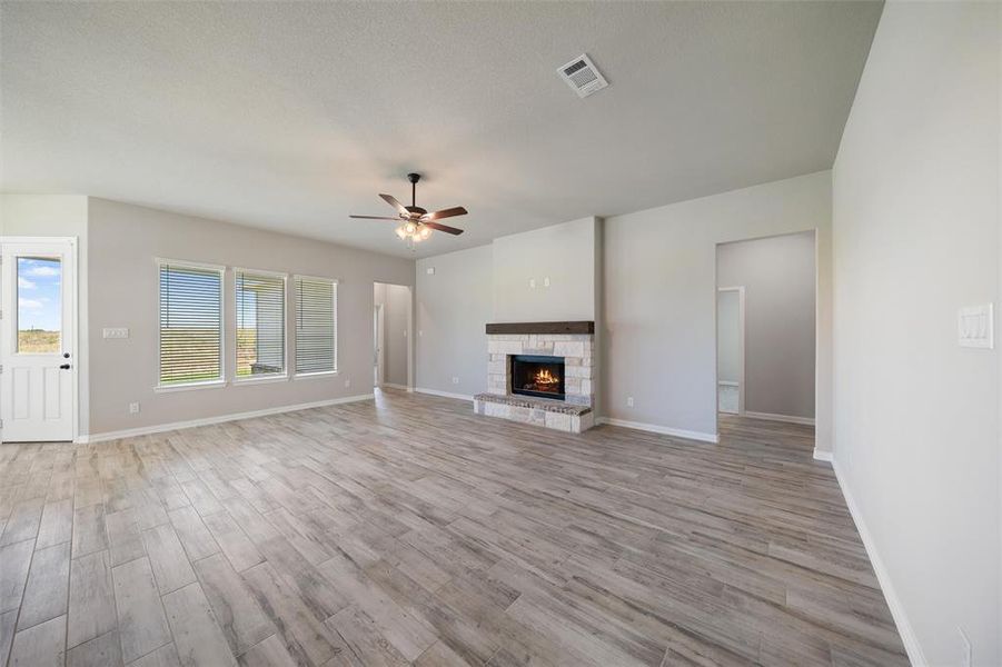 Unfurnished living room featuring a stone fireplace, light wood finished floors, and ceiling fan Unfurnished living room featuring a stone fireplace, light wood finished floors, and ceiling fan