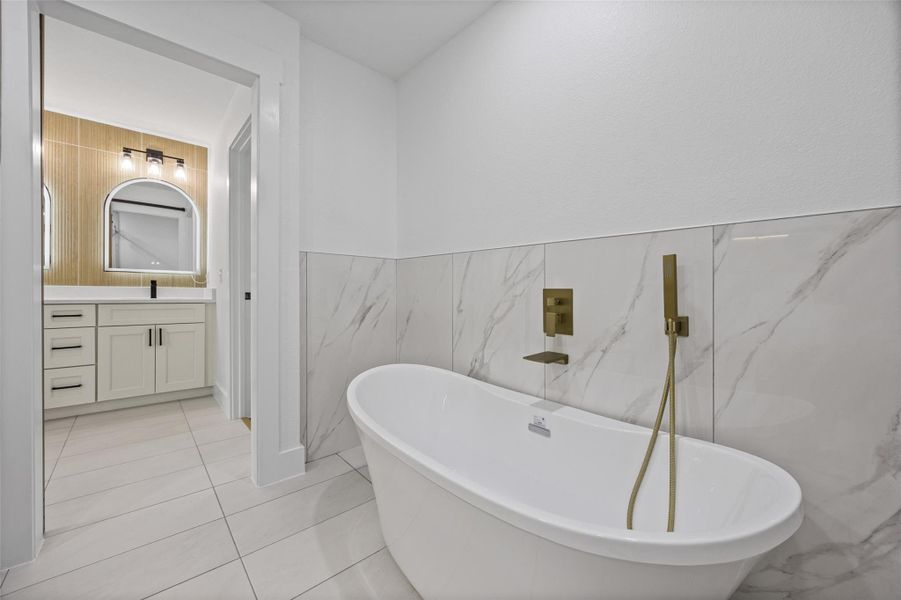 Freestanding bathtub with wall-mounted brass fixtures, set against large-format marble-look wall tiles Freestanding bathtub with wall-mounted brass fixtures, set against large-format marble-look wall tiles