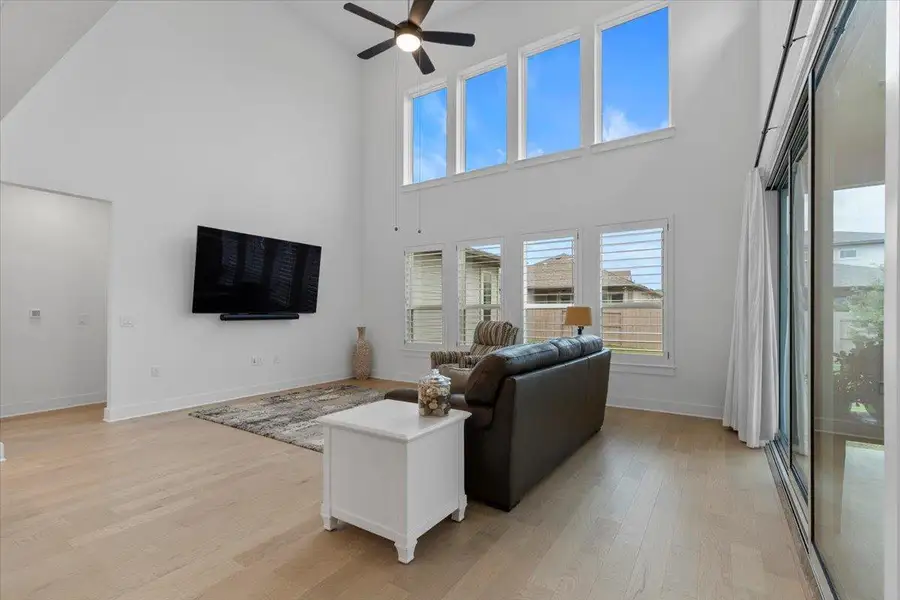 Living area with high vaulted ceiling, a ceiling fan, light wood finished floors, and healthy amount of natural light