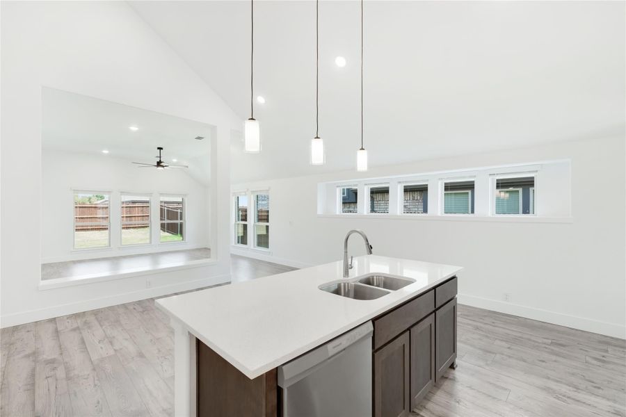 Kitchen island with double sink, dark cabinets, white countertop, and pendant lights above open floor plan with high ceilings Kitchen island with double sink, dark cabinets, white countertop, and pendant lights above open floor plan with high ceilings