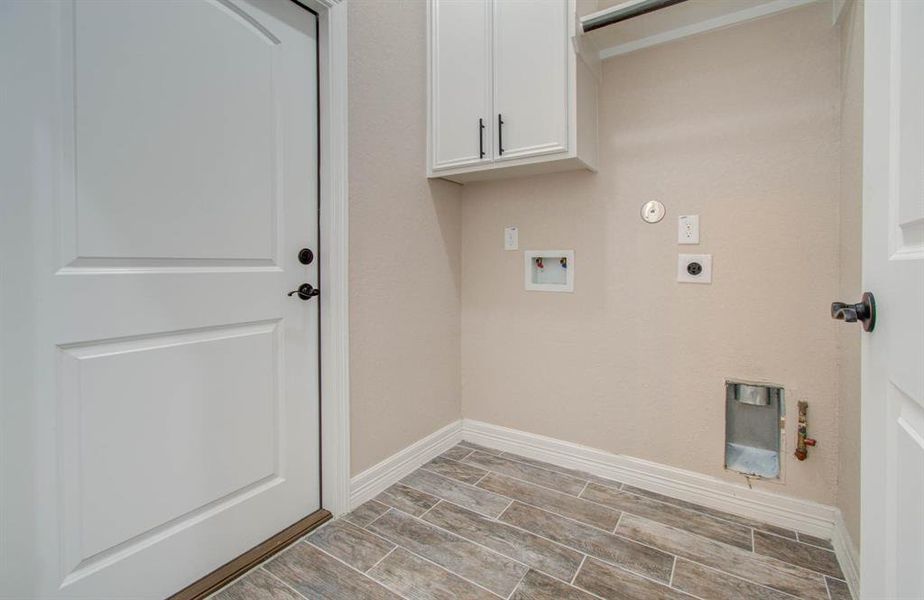 This is a modern utility area featuring tiled flooring, neutral wall colors, white cabinetry, and hookups for laundry appliances. It's a clean, compact space designed for efficiency.