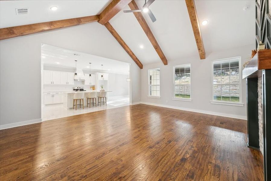 Unfurnished living room featuring beam ceiling, ceiling fan, high vaulted ceiling, and hardwood / wood-style flooring