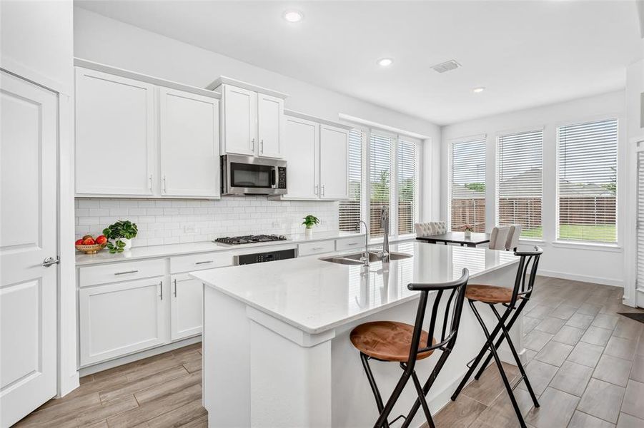 Contemporary kitchen featuring an island with a stainless steel sink, white cabinetry, a subway tile backsplash, stainless steel appliances, and wood-finish flooring