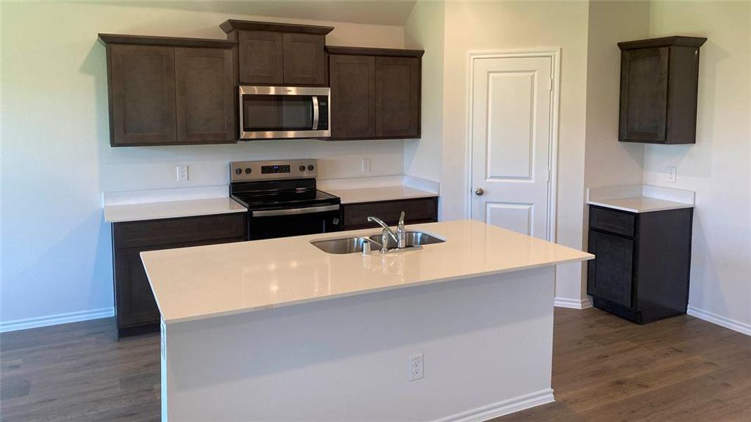 Kitchen with dark wood finish cabinets, stainless steel appliances, an island with sink, and dark wood-type flooring