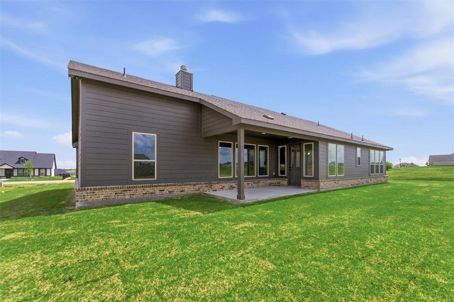 Rear view of property featuring a patio, a lawn, and brick siding