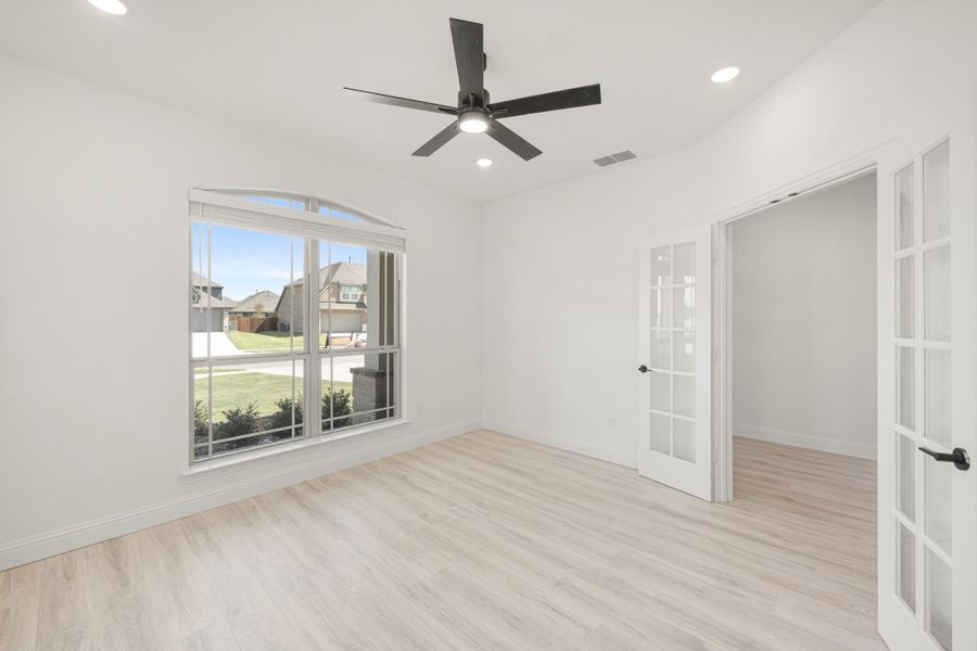 Empty room with light wood floors, ceiling fan, arched window, and French doors