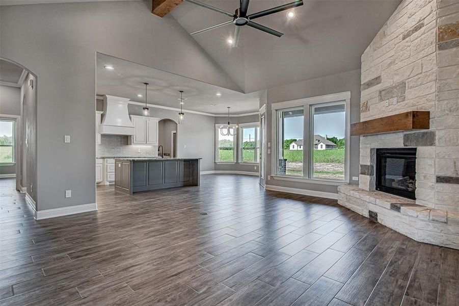 Unfurnished living room featuring beamed ceiling, a stone fireplace, sink, high vaulted ceiling, and ceiling fan