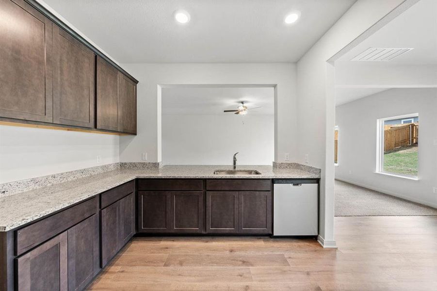 Kitchen featuring dark brown cabinets, light stone counters, dishwasher, light wood-style floors, and recessed lighting