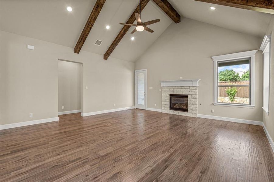 Unfurnished living room with hardwood / wood-style flooring, high vaulted ceiling, and a stone fireplace