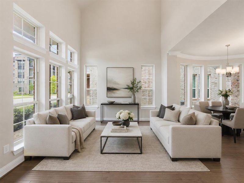 Soaring ceilings define this open living area featuring large windows with white trim, wood-finish flooring, and a dining space with a contemporary chandelier Soaring ceilings define this open living area featuring large windows with white trim, wood-finish flooring, and a dining space with a contemporary chandelier