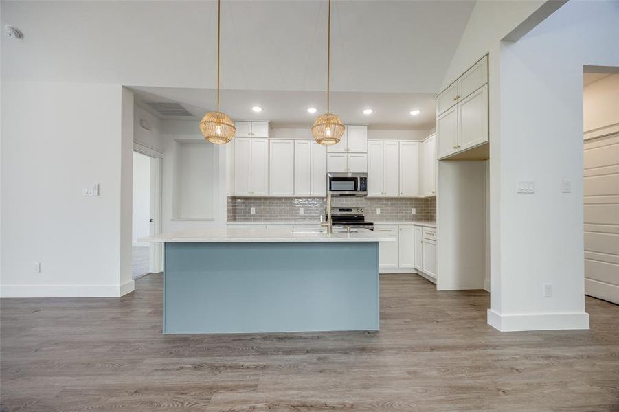 Kitchen with white cabinets, pendant lighting, an island with sink, appliances with stainless steel finishes, and light wood-type flooring