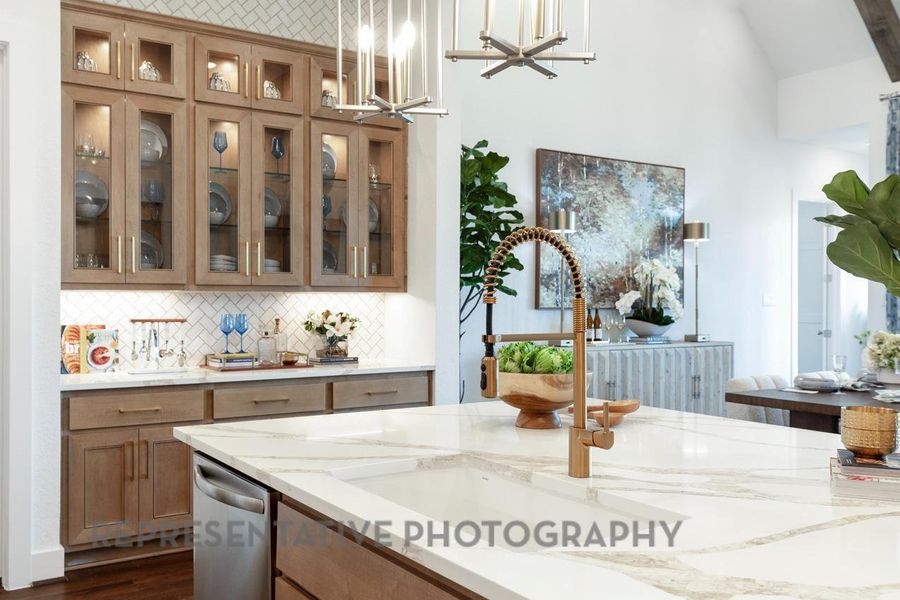 Kitchen with stainless steel dishwasher, tasteful backsplash, brown cabinetry, glass insert cabinets, and light stone countertops Kitchen with stainless steel dishwasher, tasteful backsplash, brown cabinetry, glass insert cabinets, and light stone countertops