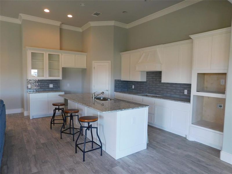 Kitchen with a center island with sink, white cabinets, crown molding, and hardwood / wood-style flooring