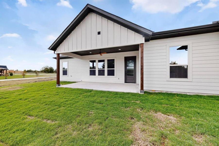 Rear view of house featuring a patio area, a yard, a ceiling fan, and board and batten siding