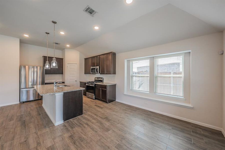 Kitchen with stainless steel appliances, dark brown cabinets, a kitchen island with sink, decorative light fixtures, and lofted ceiling Kitchen with stainless steel appliances, dark brown cabinets, a kitchen island with sink, decorative light fixtures, and lofted ceiling