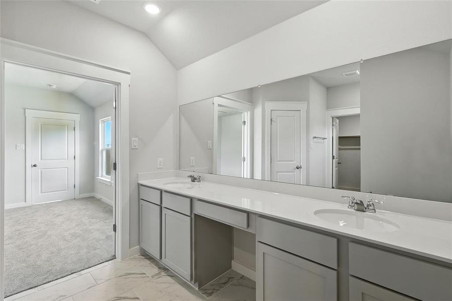 Full bath with vaulted ceiling, double vanity, marble look tiles, and recessed lighting
