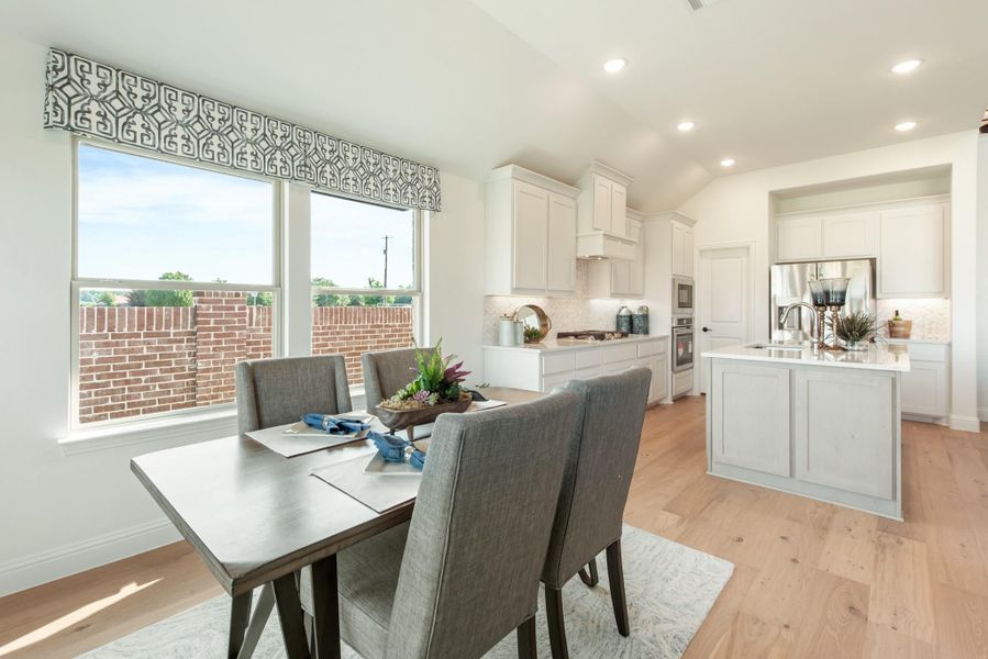Open dining area with gray chairs flows into white kitchen with island and hardwood floors Open dining area with gray chairs flows into white kitchen with island and hardwood floors