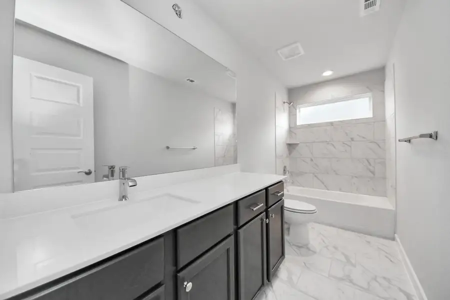 Secondary bath features tile flooring, bath/shower combo with tile surround, light stained wood cabinets, beautiful light countertop.