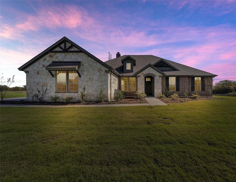 View of front of property featuring stone siding, a yard, and a chimney
