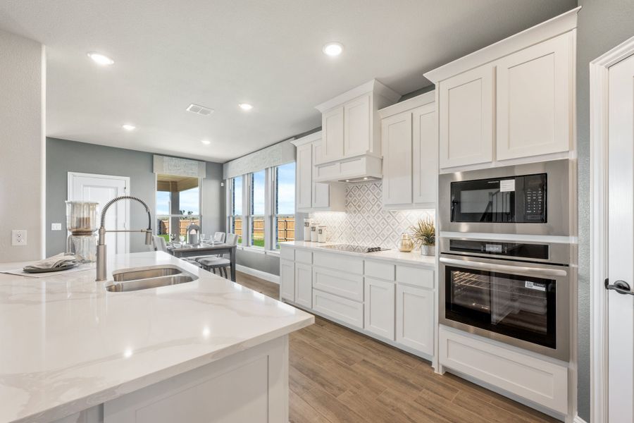 Kitchen with white cabinets, quartz island, stainless steel appliances, and tile backsplash on wood-look floors