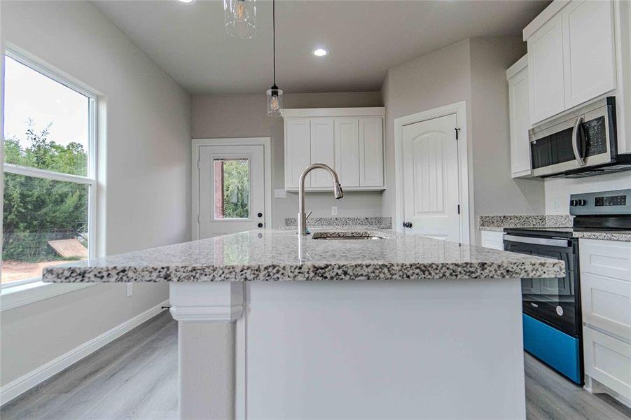 Kitchen with a healthy amount of sunlight, pendant lighting, range with electric cooktop, and a kitchen island with sink