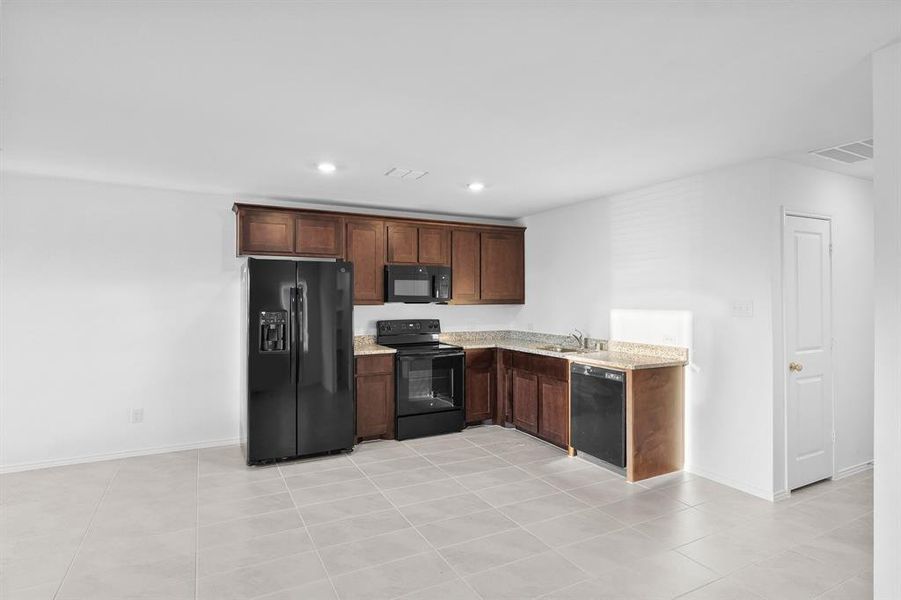 Kitchen with light tile patterned floors, light stone countertops, sink, and black appliances